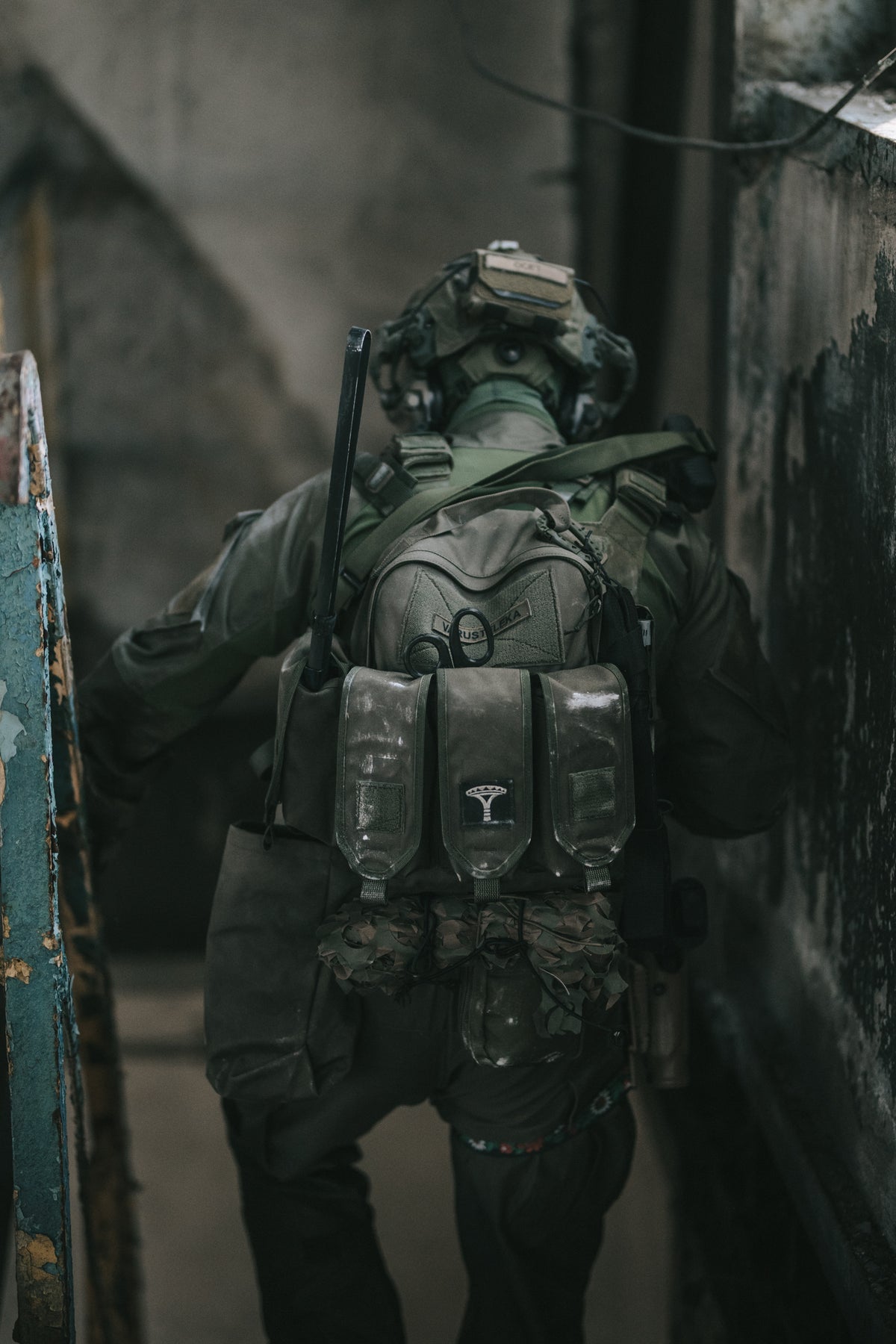 Person in tactical gear with a helmet and backpack in a dimly lit area walking down the stairs of an old building.