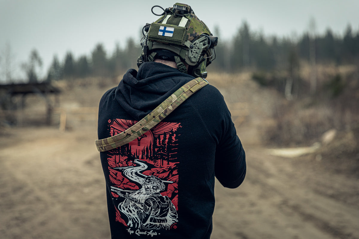 Person wearing a black hoodie with a red and white design at an outdoor shooting range.