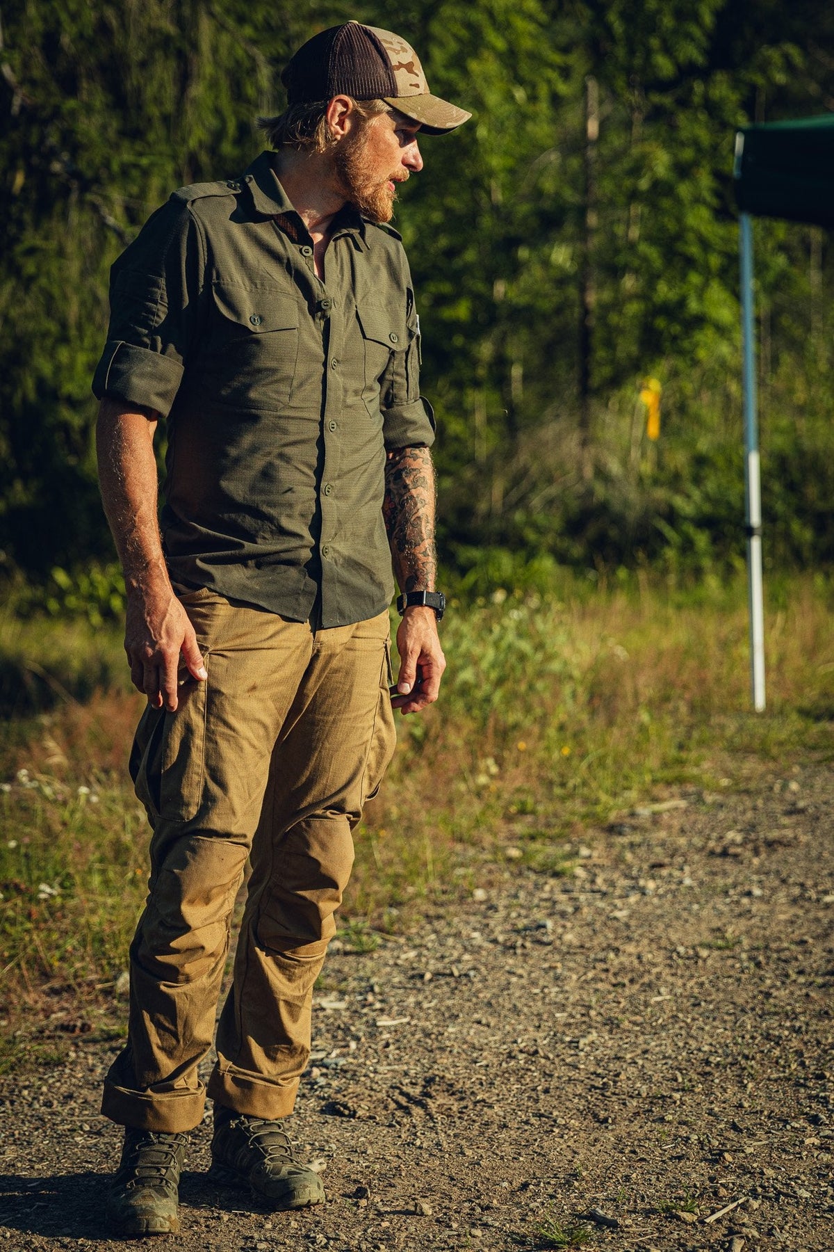 Man in outdoor attire standing on a gravel path with greenery in the background