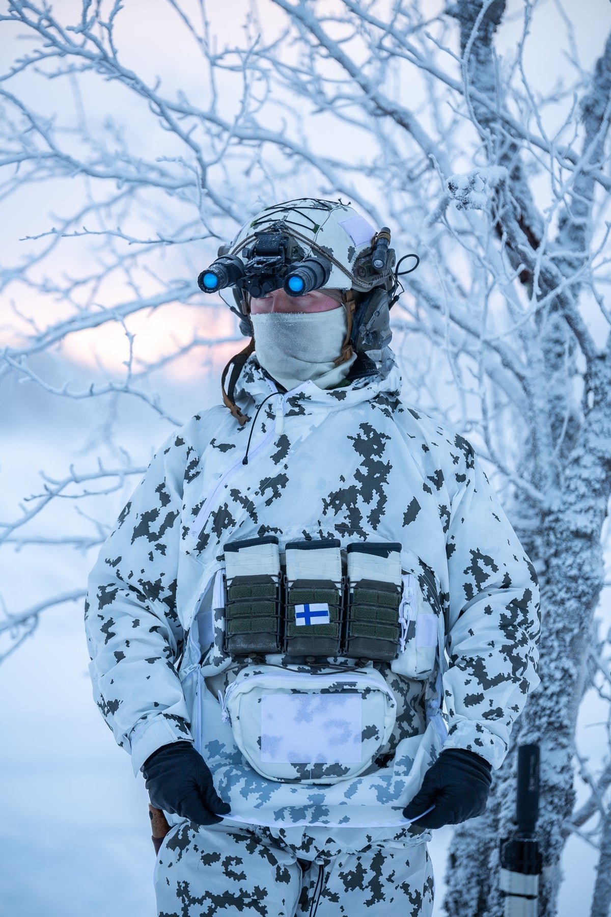 Person in winter camouflage gear with a plate carrier in a snowy forest