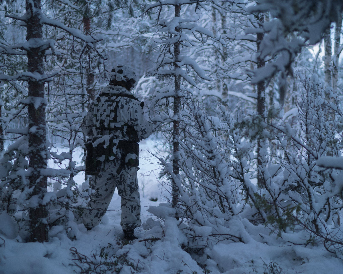 A soldier in a snowy forest wearing a helmet with white Savotta Helmet Camo Scrim.